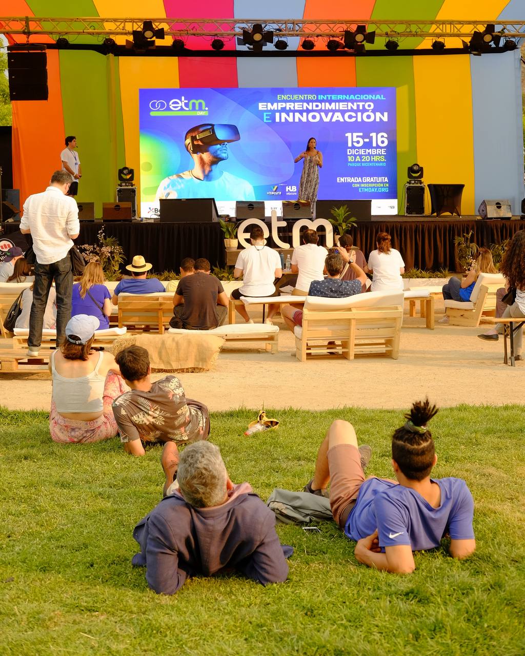 Charla en escenario, público en el pasto